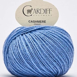 May include: A ball of light blue Cardiff Cashmere Classic yarn. The yarn is tightly wound and has a textured appearance. A tag above the yarn displays the brand name and the word "Cashmere".