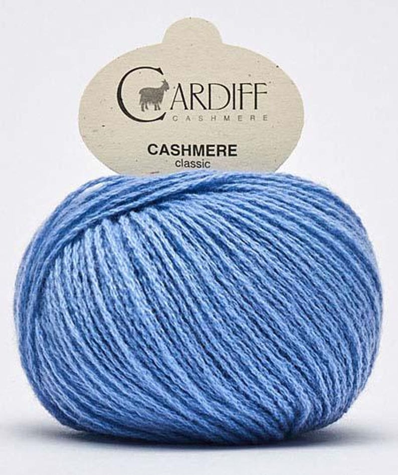 May include: A ball of light blue Cardiff Cashmere Classic yarn. The yarn is tightly wound and has a textured appearance. A tag above the yarn displays the brand name and the word "Cashmere".