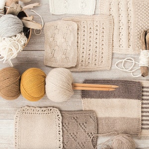 May include: An overhead shot of various knitting supplies. Several skeins of yarn in shades of white, gray, brown, and yellow are arranged with wooden knitting needles and knitted swatches. A wooden bowl holds more yarn and driftwood.