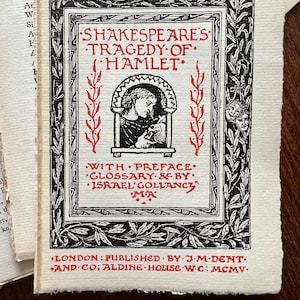 May include: A black and white illustration of a book cover for Shakespeare's Tragedy of Hamlet. The cover features a decorative border with a red title and a small illustration of a person holding a skull. The text on the cover reads "Shakespeare's Tragedy of Hamlet" and "With Preface, Glossary & by Israel Gollancy MA". The bottom of the cover reads "London: Published by J.M. Dent & Co: Aldine House W.C: MCMV."