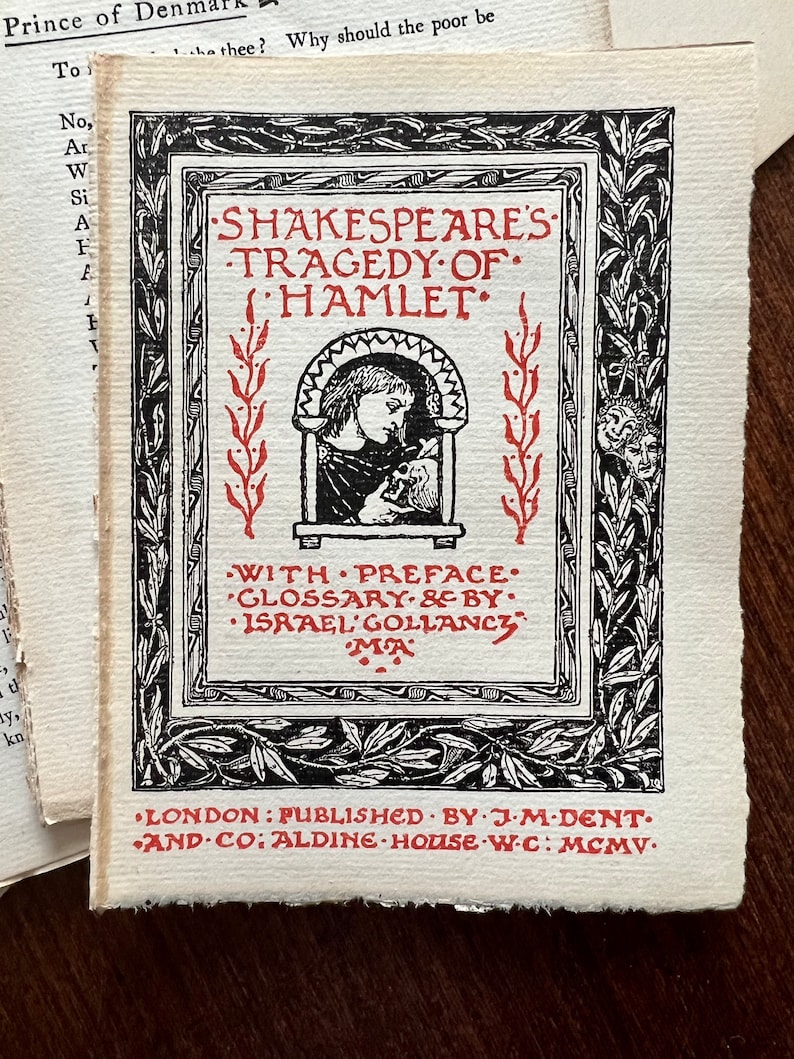May include: A black and white illustration of a book cover for Shakespeare's Tragedy of Hamlet. The cover features a decorative border with a red title and a small illustration of a person holding a skull. The text on the cover reads "Shakespeare's Tragedy of Hamlet" and "With Preface, Glossary & by Israel Gollancy MA". The bottom of the cover reads "London: Published by J.M. Dent & Co: Aldine House W.C: MCMV."