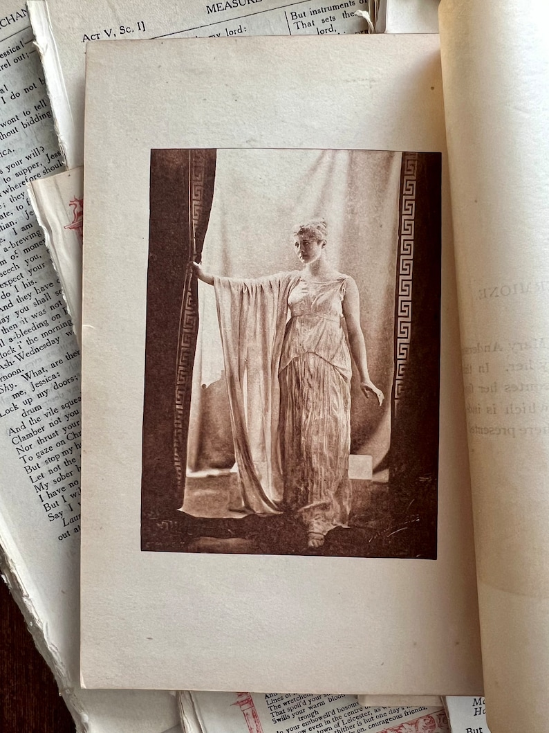 May include: A black and white photograph of a woman in a long white dress standing in a doorway. The woman is holding the edge of a curtain with her left hand and her right hand is at her side. The doorway is decorated with a geometric pattern.