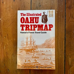 May include: A vintage travel guide book cover with the title "The Illustrated Oahu Tripmap" in red and white text. The subtitle is "Hawaii's Finest Travel Guide" in black text. The cover features a brown and white illustration of a ship sailing into a harbor.