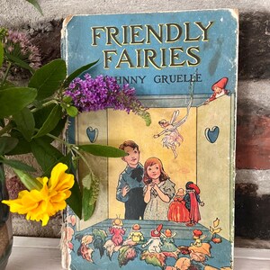 May include: Vintage children's book titled "Friendly Fairies" by Johnny Gruelle. The cover is light blue with gold lettering and illustrations of children and fairies. The book is worn, with visible signs of age.