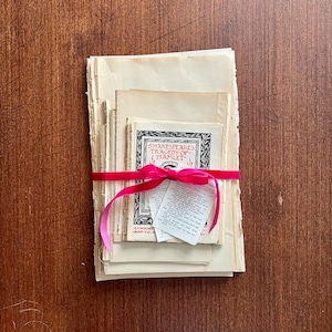 May include: A stack of vintage paperbacks tied together with a pink ribbon. The top book has the title "Shakespeare's Tragedy of Hamlet" printed on the cover.