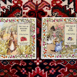 May include: Two square pop-up books by Beatrix Potter. The left book is titled The Tale of Benjamin Bunny, featuring a rabbit in a garden. The right book is titled The Tale of Tom Kitten, showing kittens in a garden. Both have floral borders.