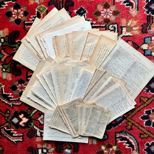 May include: A collection of vintage, off-white, paper pages with printed text, arranged in a fan shape on a red and black patterned rug.