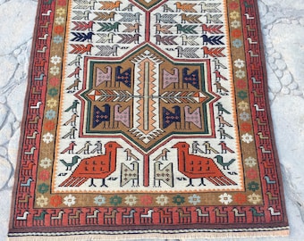 May include: A rectangular woven rug featuring a central geometric star motif surrounded by repeating bird patterns in shades of red, blue, green, and brown on a cream background, with a decorative border of small animal figures and floral shapes.
