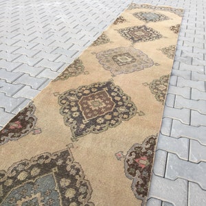 Pu&ograve; includere: Un tappeto da corridoio beige con un designo persiano tradizionale. Il tappeto presenta un motivo a rombi con dettagli intricati in tonalit&agrave; di marrone, verde e blu.