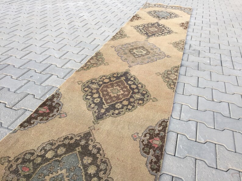 Pu&ograve; includere: Un tappeto da corridoio beige con un designo persiano tradizionale. Il tappeto presenta un motivo a rombi con dettagli intricati in tonalit&agrave; di marrone, verde e blu.