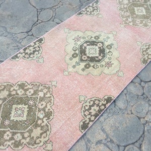May include: A pink and brown patterned runner rug with a geometric design. The rug has a distressed look and is made of a soft, woven material.