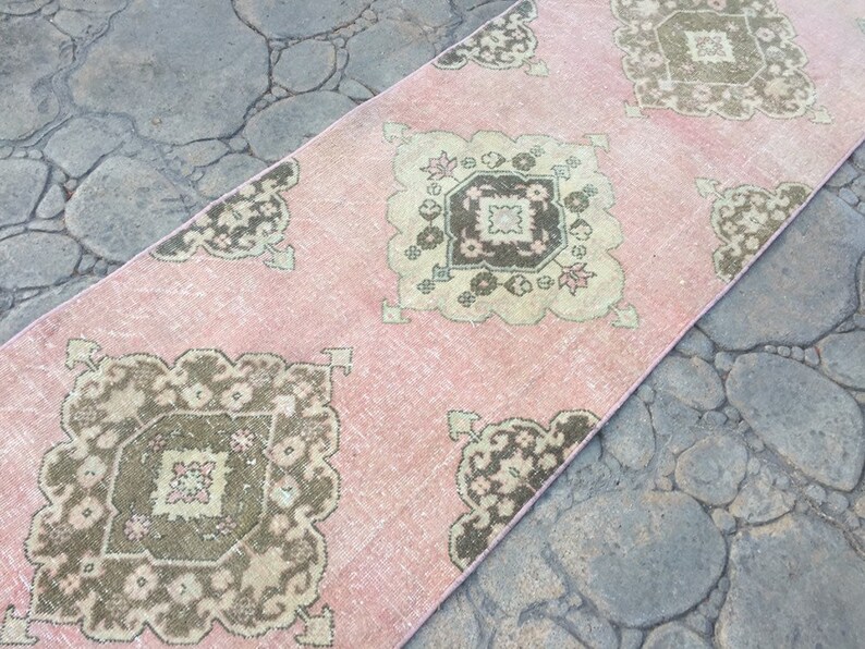 May include: A pink and brown patterned runner rug with a geometric design. The rug has a distressed look and is made of a soft, woven material.