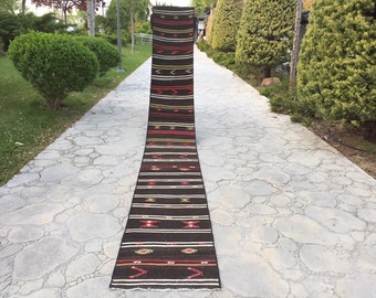 May include: A long, narrow, black and red rug with a geometric pattern. The rug is laid out on a stone path.