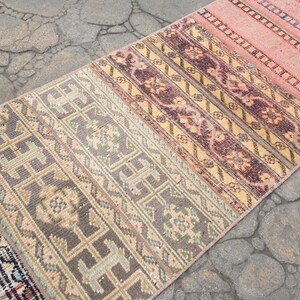 May include: A long, narrow rug with a multi-colored striped pattern. The rug has a faded, vintage look and is made of woven fabric. The colors include shades of pink, beige, brown, and gray.