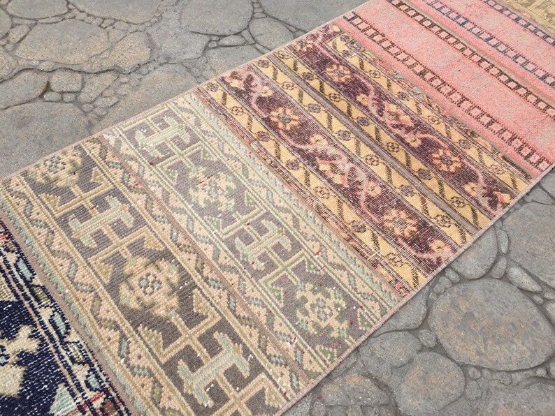 May include: A long, narrow rug with a multi-colored striped pattern. The rug has a faded, vintage look and is made of woven fabric. The colors include shades of pink, beige, brown, and gray.
