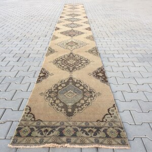 Pu&ograve; includere: Un tappeto da corridoio lungo e beige con un design persiano tradizionale. Il tappeto presenta un motivo floreale marrone scuro e blu con un bordo verde e marrone.