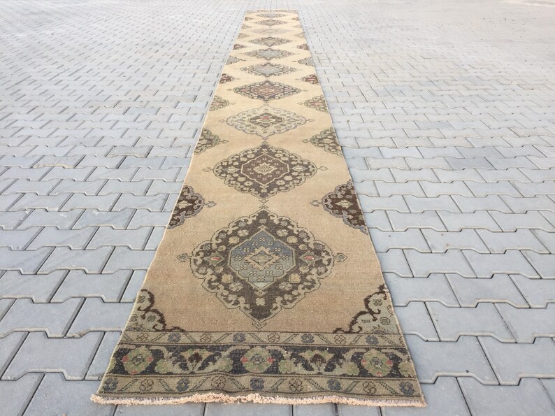 Pu&ograve; includere: Un tappeto da corridoio lungo e beige con un design persiano tradizionale. Il tappeto presenta un motivo floreale marrone scuro e blu con un bordo verde e marrone.