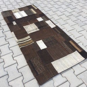 May include: A rectangular patchwork rug featuring a mix of brown, beige, and white fabric squares. The rug's design incorporates various textures and shades of brown, giving it a rustic look. The rug is approximately 152 cm long.