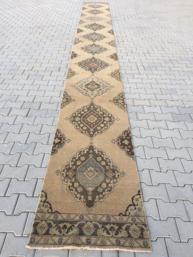 Pu&ograve; includere: Un tappeto da corridoio lungo e beige con un design persiano tradizionale. Il tappeto presenta motivi intricati in tonalit&agrave; di marrone, blu e verde. Il tappeto ha un bordo con frange.