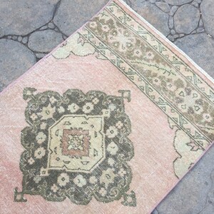 May include: A pink and green vintage rug with a geometric pattern. The rug has a faded look and is made of wool.