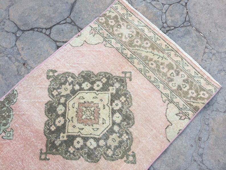 May include: A pink and green vintage rug with a geometric pattern. The rug has a faded look and is made of wool.