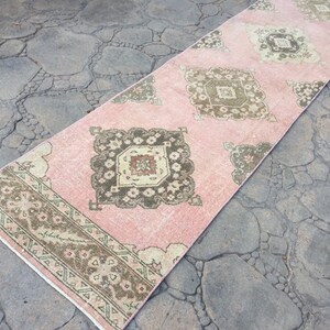 May include: A pink and brown patterned runner rug with a geometric design. The rug has a faded, vintage look.