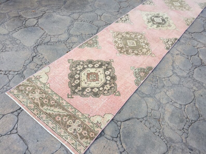 May include: A pink and brown patterned runner rug with a geometric design. The rug has a faded, vintage look.