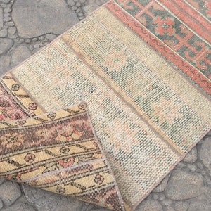 May include: A vintage rug with a cream background and colorful geometric patterns. The rug is folded in half, revealing a brown and cream patterned underside.