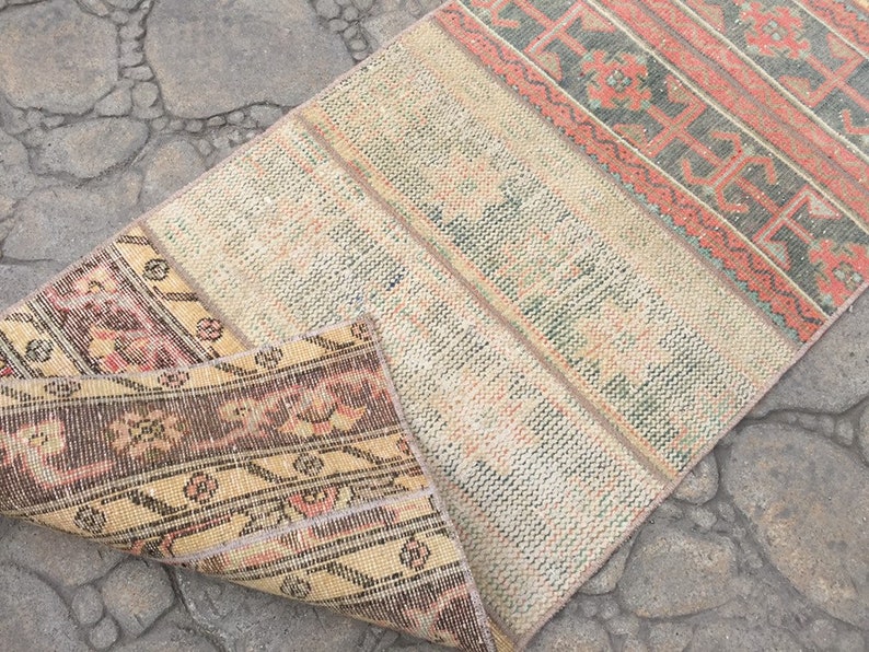 May include: A vintage rug with a cream background and colorful geometric patterns. The rug is folded in half, revealing a brown and cream patterned underside.