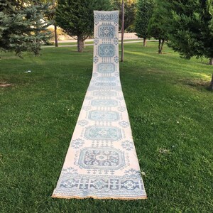 May include: A long, white runner rug with a blue and white geometric pattern. The rug is laid out on a grassy lawn.