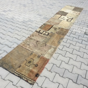 Könnte beinhalten: Ein langer, rechteckiger Teppich aus Patchwork-Stücken aus verschiedenen farbigen und gemusterten Stoffen. Der Teppich ist eine Mischung aus Beige, Braun und Creme mit einem geometrischen Muster.