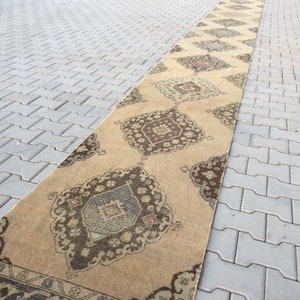 Pu&ograve; includere: Un tappeto da corridoio beige con un motivo geometrico marrone e blu. Il tappeto ha un design tradizionale con dettagli intricati.