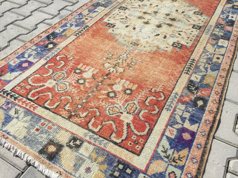 May include: A vintage Turkish runner rug with a red, orange, and blue geometric pattern. The rug has a faded, distressed look and features a central medallion design.