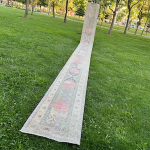 May include: A long, cream-coloured rug with a pink and green floral pattern. The rug is laid out on a grassy lawn.
