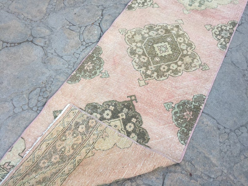 May include: A pink and green vintage rug with a floral pattern. The rug is folded in half and has a distressed look.