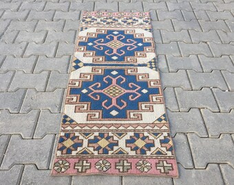 May include: A long, narrow rug with a geometric pattern in shades of blue, pink, and beige. The rug has a traditional, hand-woven look.
