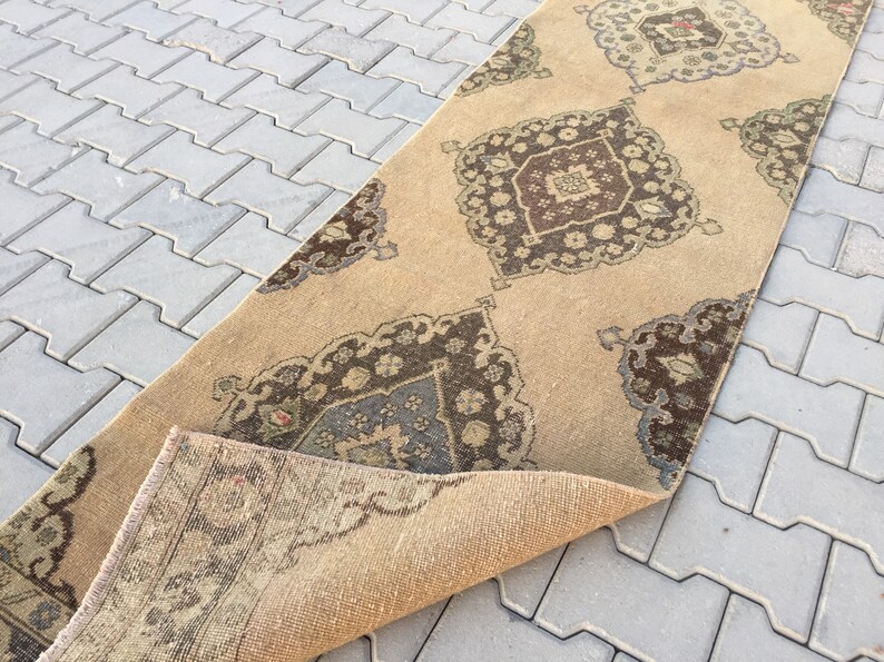 Pu&ograve; includere: Un tappeto da corridoio beige con un designo persiano tradizionale che presenta motivi intricati in tonalit&agrave; di marrone, beige e blu. Il tappeto &egrave; piegato a met&agrave;, rivelando il lato inferiore.