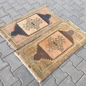 May include: Two small, rectangular rugs with a geometric pattern in shades of brown, green, and beige. The rugs have a fringe border.