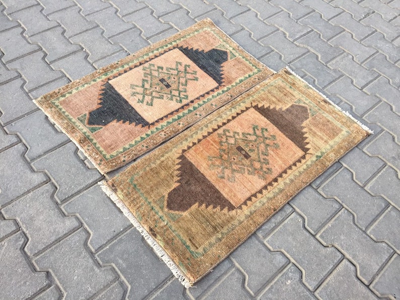 May include: Two small, rectangular rugs with a geometric pattern in shades of brown, green, and beige. The rugs have a fringe border.