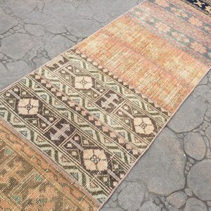 May include: A vintage runner rug with a patchwork design featuring geometric patterns in shades of brown, beige, and cream. The rug has a distressed look and is made of woven fabric.