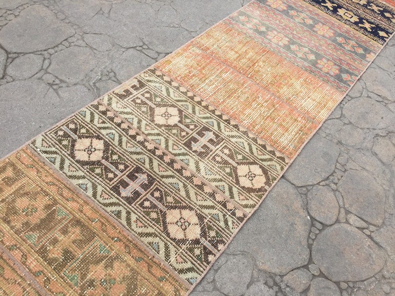 May include: A vintage runner rug with a patchwork design featuring geometric patterns in shades of brown, beige, and cream. The rug has a distressed look and is made of woven fabric.