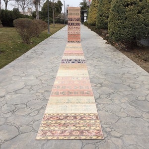 May include: A collection of colorful vintage rugs laid out on a stone walkway. The rugs are in various shades of pink, orange, yellow, and blue, with intricate patterns and designs.