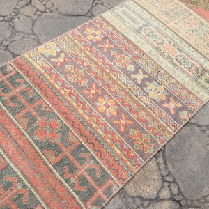 May include: A colorful vintage rug with a geometric pattern in shades of red, orange, yellow, green, and blue. The rug is made of woven fabric and has a distressed look.