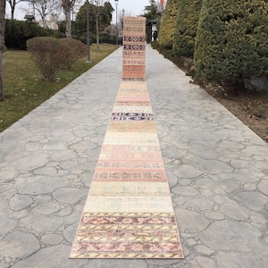 Puede incluir: Una colección de alfombras turcas vintage dispuestas en un camino de piedra. Las alfombras son de varios tonos de rosa, beige y crema con intrincados patrones.
