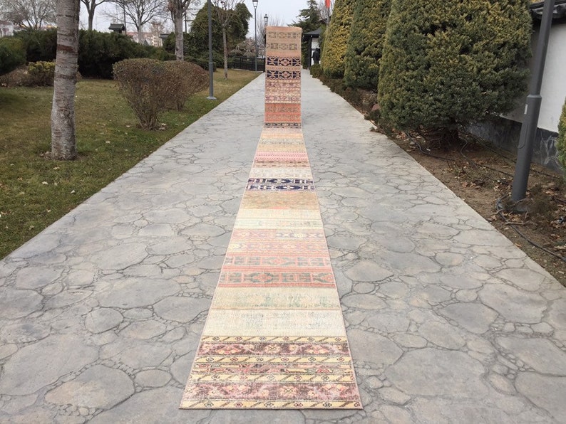 May include: A collection of vintage Turkish runner rugs laid out on a stone pathway. The rugs are in various shades of pink, beige, and cream with intricate patterns.