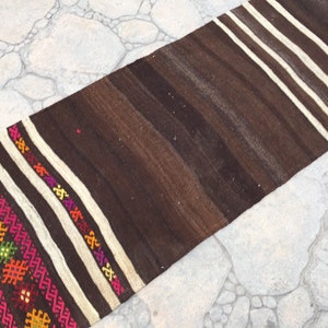 Puede incluir: Una alfombra de rayas marrones y blancas con coloridos patrones geom&eacute;tricos tejidos en el borde. La alfombra est&aacute; hecha de lana y tiene un dise&ntilde;o tradicional.