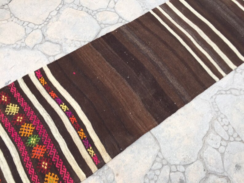 Puede incluir: Una alfombra de rayas marrones y blancas con coloridos patrones geom&eacute;tricos tejidos en el borde. La alfombra est&aacute; hecha de lana y tiene un dise&ntilde;o tradicional.