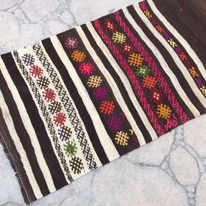 Puede incluir: Una alfombra de rayas marrones y blancas con patrones geom&eacute;tricos coloridos tejidos en el dise&ntilde;o. La alfombra tiene flecos en los bordes.