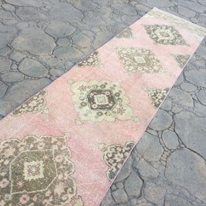 May include: A long, pink runner rug with a traditional Persian design in shades of brown and beige. The rug has a faded, vintage look and is perfect for adding a touch of bohemian style to any room.