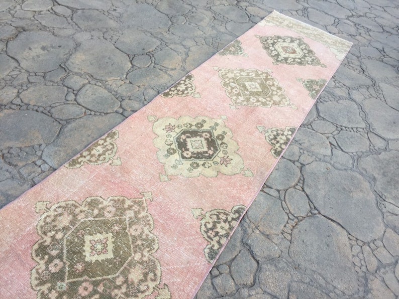 May include: A long, pink runner rug with a traditional Persian design in shades of brown and beige. The rug has a faded, vintage look and is perfect for adding a touch of bohemian style to any room.